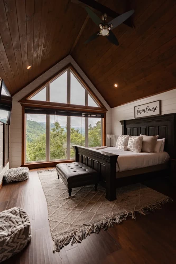 A vaulted farmhouse master bedroom with a peaked mountain-view window, freshly turned over